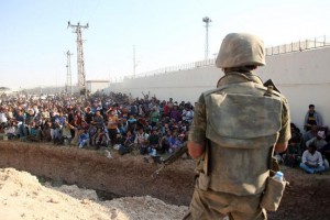 Turkish soldiers stand guard along the Syria/Turkey border while thousands of refugees look on - Photo: Ebrahem Khadir/ UPI 