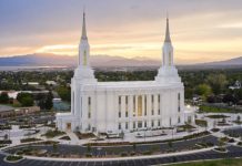 White temple with two towers on a hill, set against a sunset over a valley and freeway parking lot nearby.