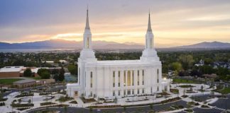 White temple with two towers on a hill, set against a sunset over a valley and freeway parking lot nearby.