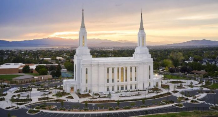 White temple with two towers on a hill, set against a sunset over a valley and freeway parking lot nearby.