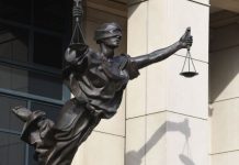 Bronze statue of Lady Justice holding scales with one arm raised, blindfolded, on a building façade.