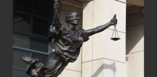 Bronze statue of Lady Justice holding scales with one arm raised, blindfolded, on a building façade.