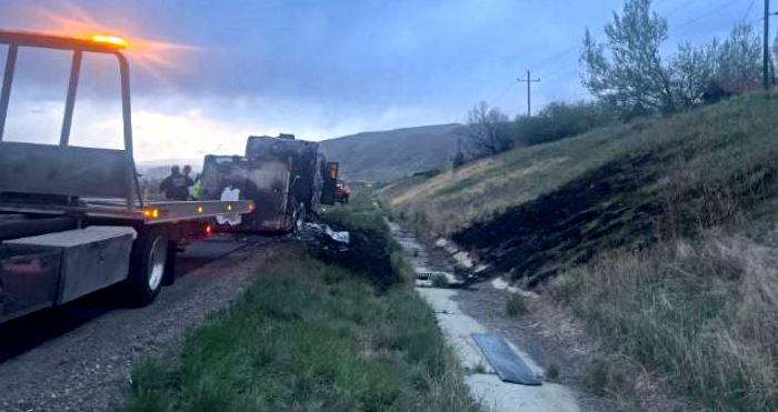 Tow truck with flashing amber light on a rural road as responders assess a wreck and debris near a ditch/creek.