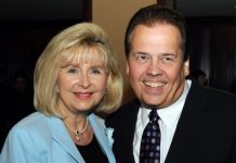 Smiling man in a dark suit and a woman in a light blue blazer pose together at a formal event.