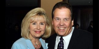 Smiling man in a dark suit and a woman in a light blue blazer pose together at a formal event.