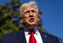 Trump says U.S. may bomb Iran if it doesn’t follow peace plan Man in a navy suit and red tie speaking outdoors against a blue sky and green trees in the background.