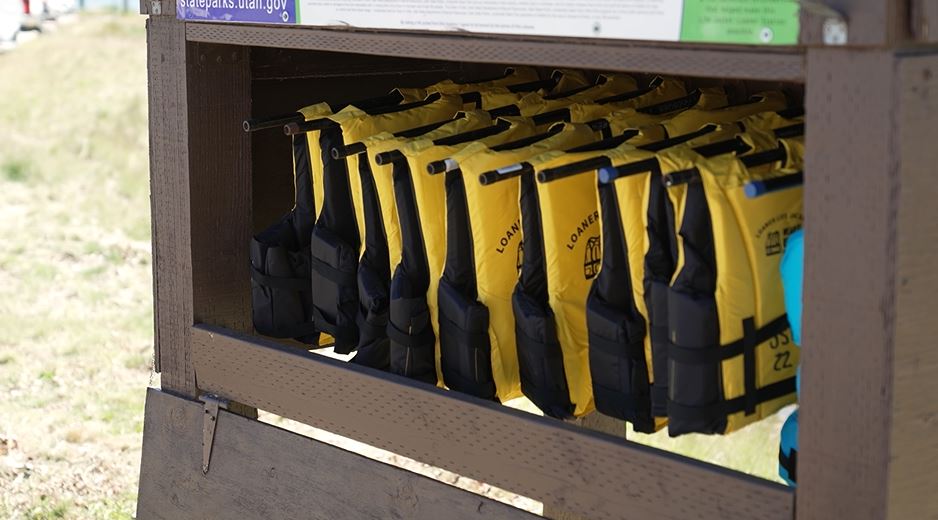 Row of yellow life jackets in a wooden rack outdoors, ready for wear for water safety.