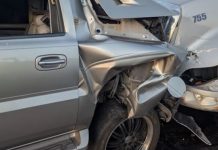 Silver pickup truck with heavy front-end damage from a collision with a large gray truck, driver-side area crumpled and wheel exposed