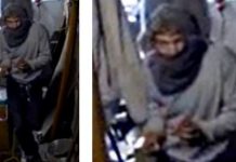 Person wearing a gray hijab and robe standing in a dim transit vehicle, looking down while adjusting their hands.