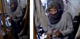 Person wearing a gray hijab and robe standing in a dim transit vehicle, looking down while adjusting their hands.