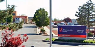Intermountain Health Cedar City Hospital sign in a parking lot with trees and a hospital entrance in the background.