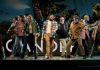 Diverse group of people dancing on a stage, performing a coordinated routine with a colorful backdrop behind them.