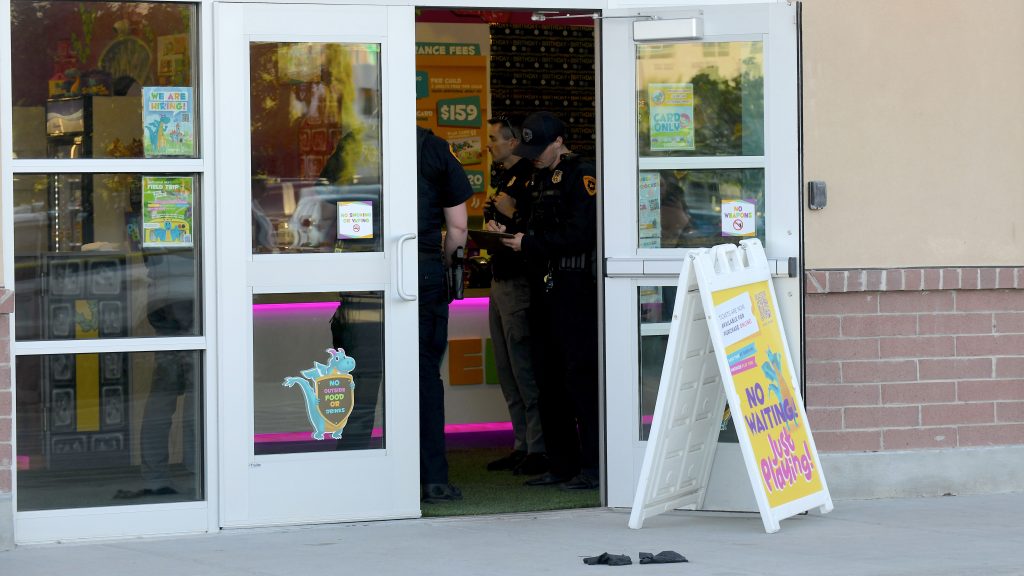 Two police officers inside a store doorway talking to a man; posters on glass doors and a yellow 'No waiting' sign outside.