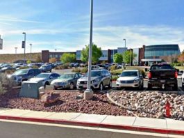 Desert Hills shopping center parking lot with cars and a storefront sign in the foreground on a sunny day.ka?