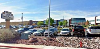Desert Hills shopping center parking lot with cars and a storefront sign in the foreground on a sunny day.ka?