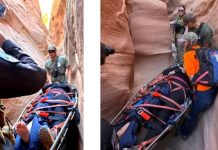 Rescue team carries an injured person on a backboard through a narrow slot canyon, secured with red straps.