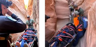 Rescue team carries an injured person on a backboard through a narrow slot canyon, secured with red straps.