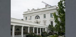 White neoclassical building with a long colonnaded veranda, arched windows, and a garden in front.