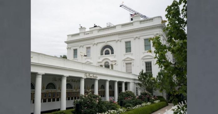 White neoclassical building with a long colonnaded veranda, arched windows, and a garden in front.