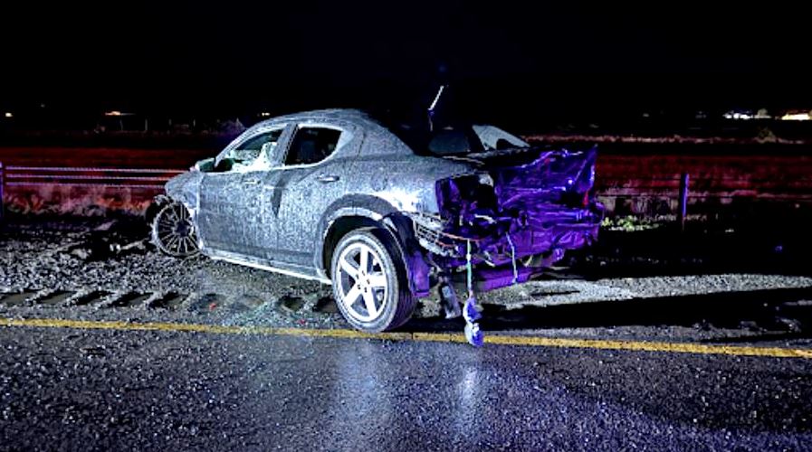 Silver SUV with significant rear end damage sits on a wet highway at night debris scattered around the road after a crash