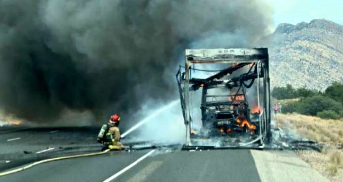 Hurricane 6 Firefighter spraying water on a burned bus on a highway with heavy smoke and mountains in the background.