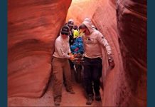 Rescue team carries a person on a stretcher through a narrow red sandstone slot canyon.