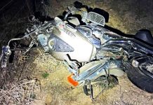Motorcycle wreck on its side in a dirt area, headlight exposed and front fairing damaged at night.