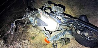 Motorcycle wreck on its side in a dirt area, headlight exposed and front fairing damaged at night.