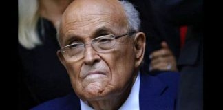 Older man with glasses in a blue suit, frowning slightly and looking to the side.
