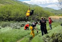 Mountain biker rescued after crash, injuries Rescue team outdoors on a grassy hillside; one person rappelling down with a rope while others assist and observe.