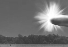 Pentagon announces release of 162 unidentified object files Grayscale landscape showing a bright sunburst on the right, rays radiating across the sky over a tree line and open field; a small rectangular object sits in the foreground left of center.