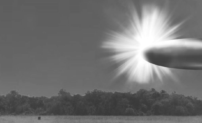 Grayscale landscape showing a bright sunburst on the right, rays radiating across the sky over a tree line and open field; a small rectangular object sits in the foreground left of center.