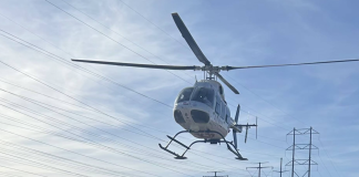 White helicopter hovering above power lines against a blue sky.