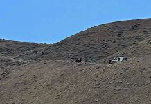 White SUV parked on a rocky hillside under a blue sky.