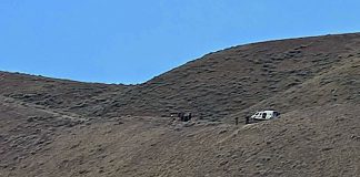 White SUV parked on a rocky hillside under a blue sky.
