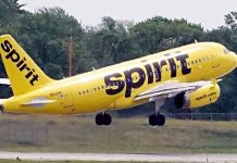 Bright yellow Spirit Airlines plane lifting off the runway, landing gear still down, with 'Spirit' branding on the fuselage.