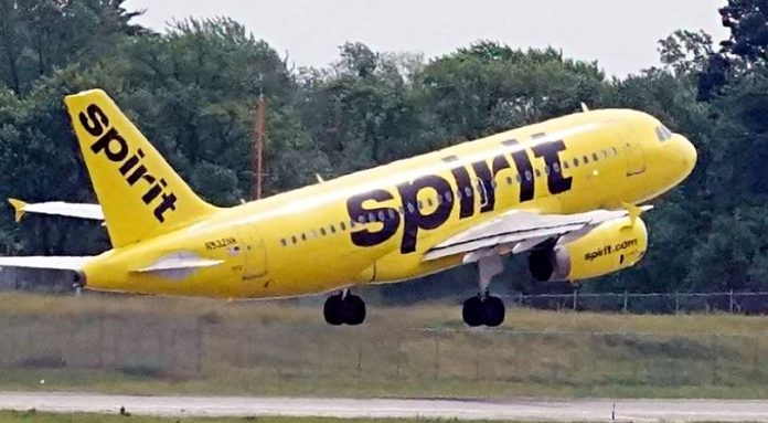 Bright yellow Spirit Airlines plane lifting off the runway, landing gear still down, with 'Spirit' branding on the fuselage.