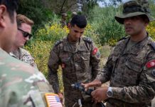 Two U.S. Army soldiers reported missing in Morocco Group of soldiers in camouflage uniforms examining a handheld device outdoors in a field of wildflowers and shrubs.