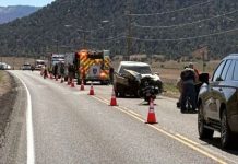 Emergency responders and vehicles on a highway scene with orange traffic cones around a motorcycle crash.