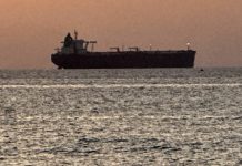 Cargo ship silhouetted on the horizon during sunset over the calm sea.