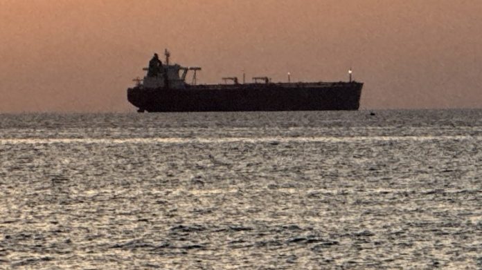 Cargo ship silhouetted on the horizon during sunset over the calm sea.