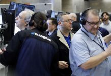 Traders wearing headsets work at computer desks in a busy trading floor.