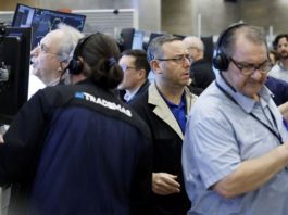 Traders wearing headsets work at computer desks in a busy trading floor.