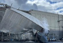 Collapsed metallic ducting leans against an industrial building, with steam rising from the wreck and debris scattered nearby.