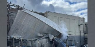 Collapsed metallic ducting leans against an industrial building, with steam rising from the wreck and debris scattered nearby.