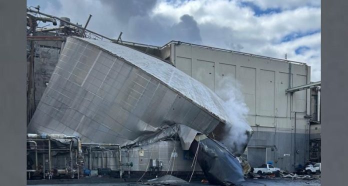 Collapsed metallic ducting leans against an industrial building, with steam rising from the wreck and debris scattered nearby.