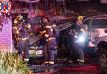 Weber Fire shares more details about Hooper garage, house fire Firefighters in full gear work at a car fire outside a brick building, with a damaged SUV and a hose on the ground outside.