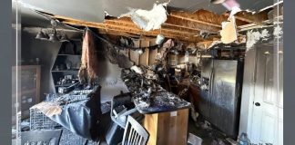 Charred kitchen with a collapsed ceiling and burnt debris strewn across a table and chairs after a house fire, showing extensive damage outside of frame edges.