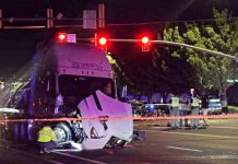 Nighttime accident scene with a damaged white semi-truck at an intersection, orange police tape, and responders in reflective vests nearby.