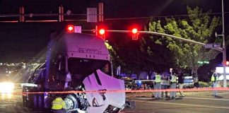 Nighttime accident scene with a damaged white semi-truck at an intersection, orange police tape, and responders in reflective vests nearby.